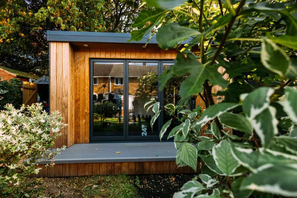Timber garden building with glazed double doors, viewed through surrounding foliage
