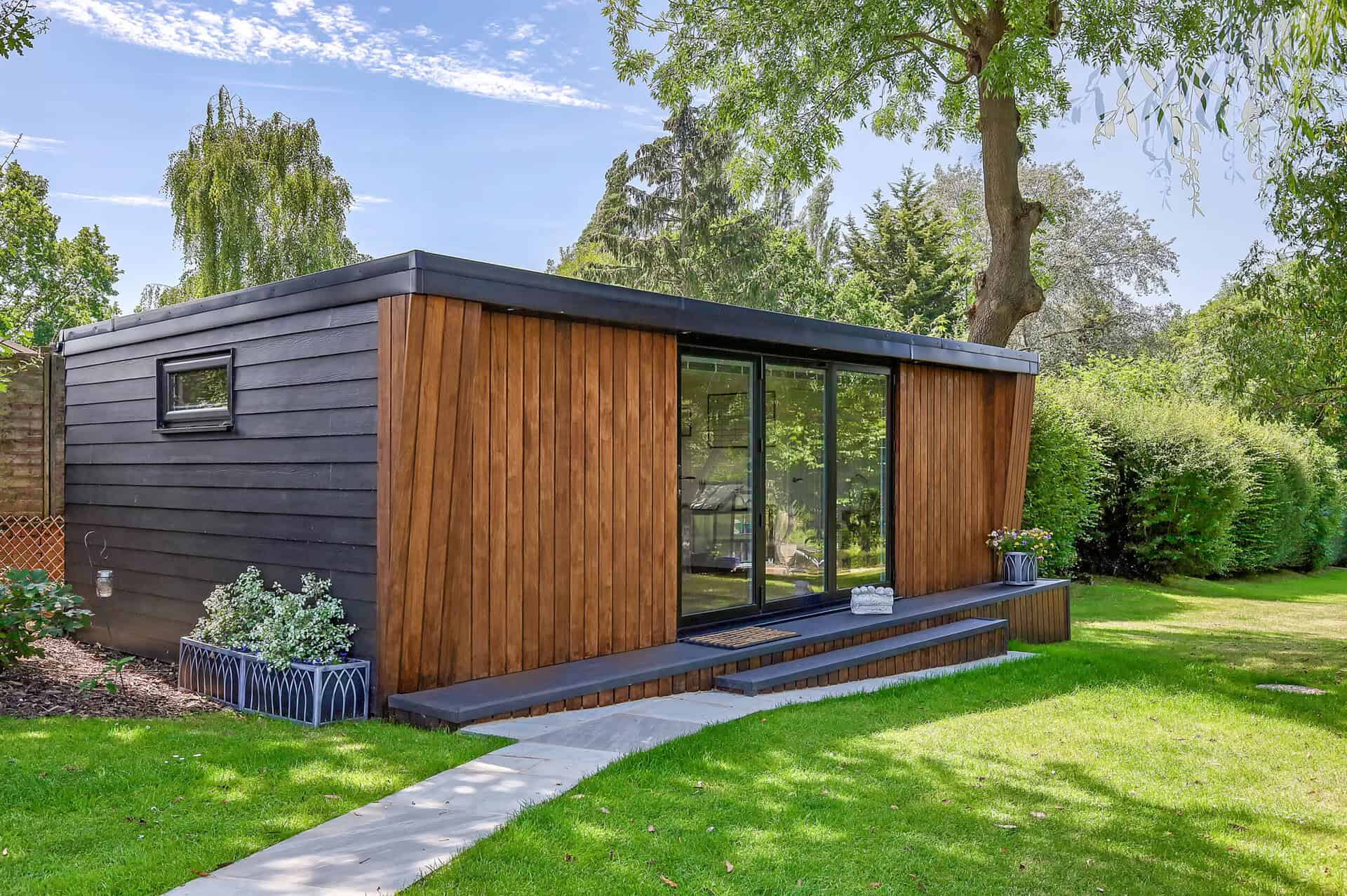 Modern garden room with dark cladding, timber doors and surrounding lawn and planting