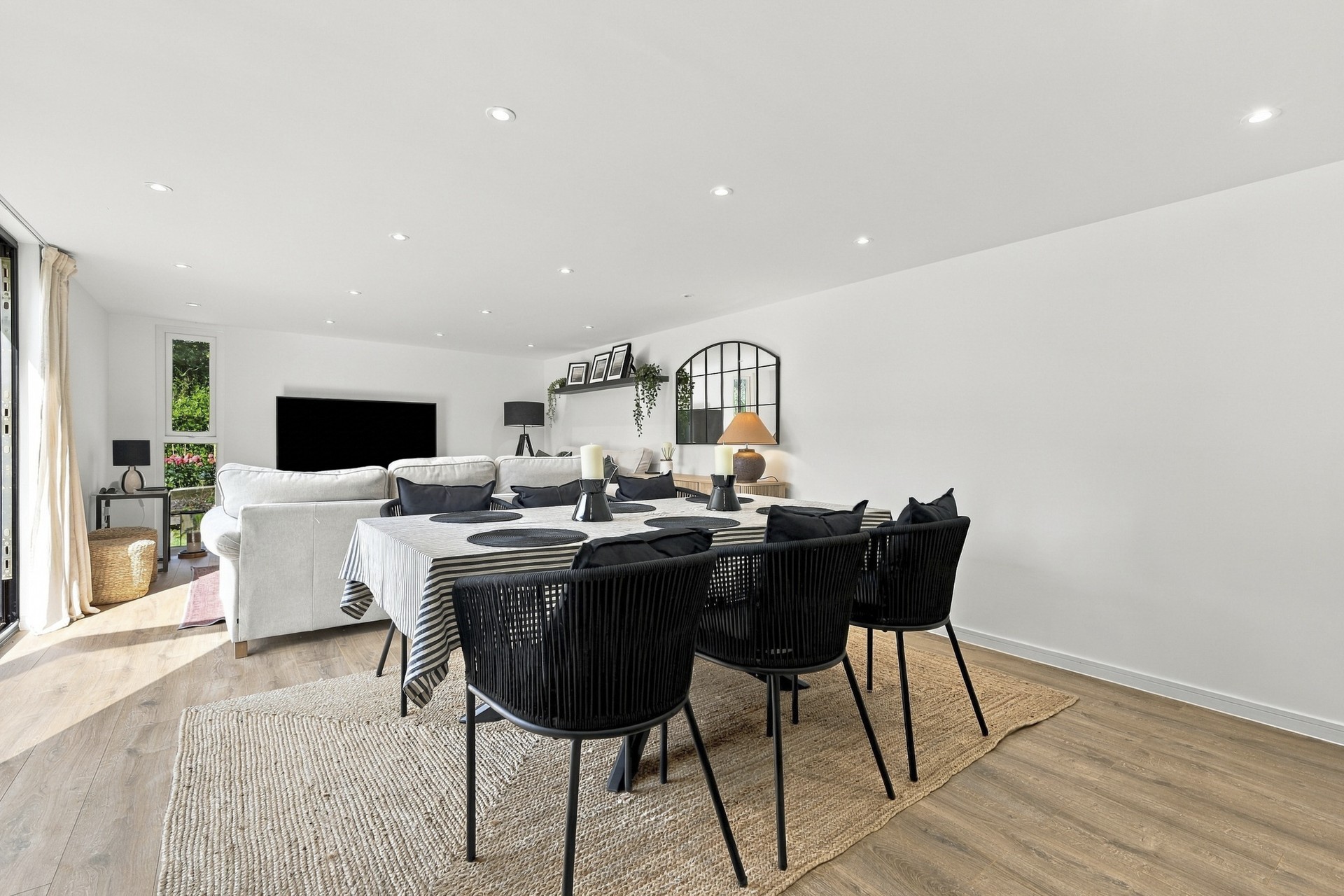 hungerdown-garden-room-dining-area-lounge-view View past the Hungerdown dining table and black chairs towards cream sofas, a television and an arched wall mirror.